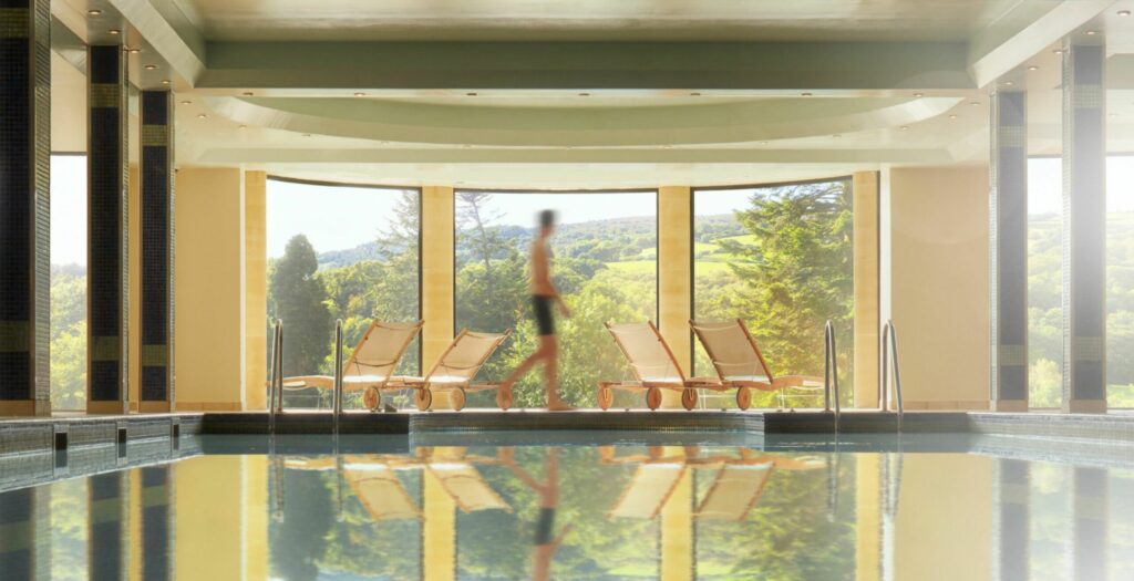 Bovey Castle spa retreat showing a person walking by a large pool and windows overlooking Dartmoor